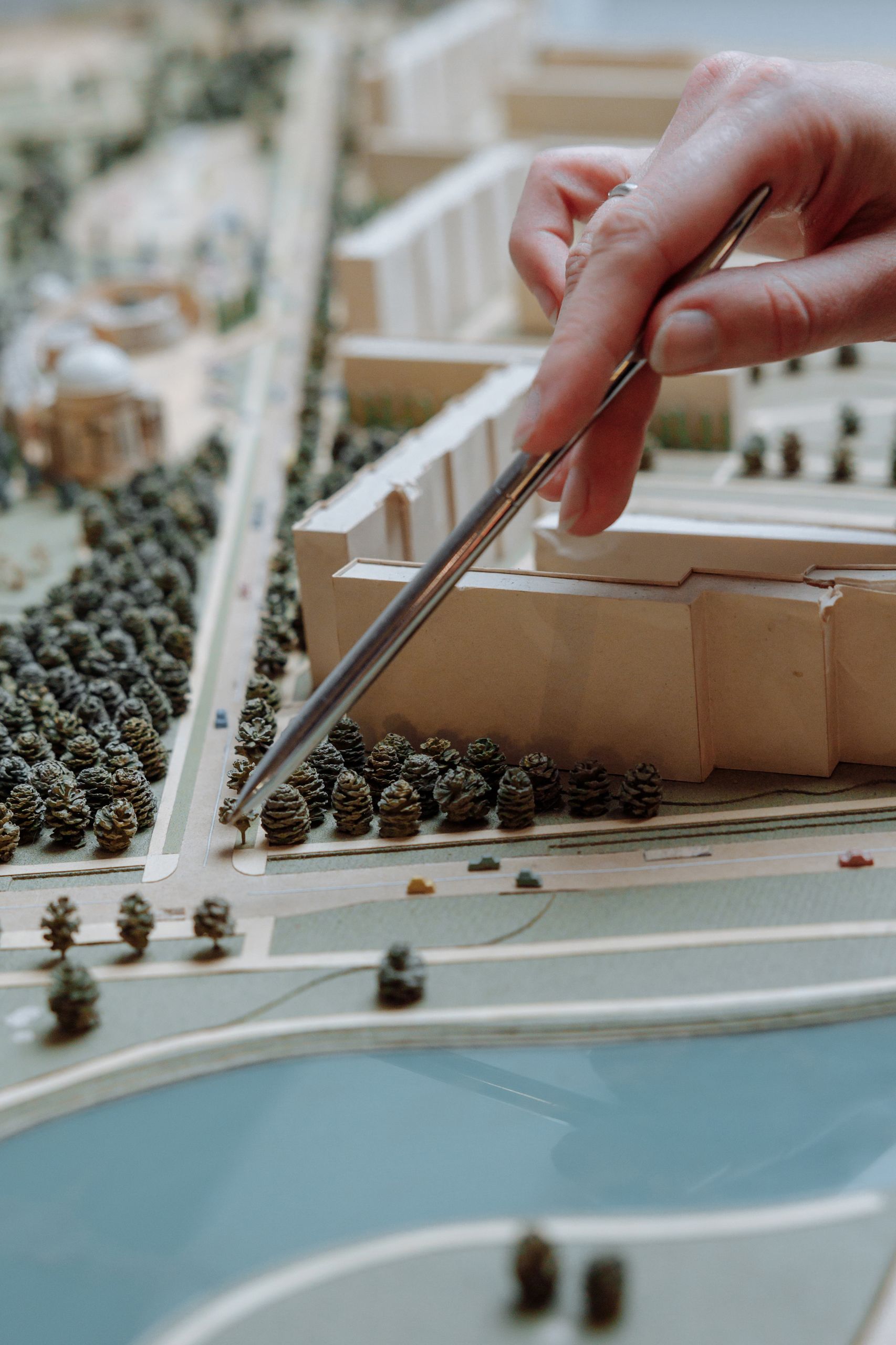 A detailed close-up of a hand using tweezers to adjust a miniature architectural model, showcasing urban planning design.